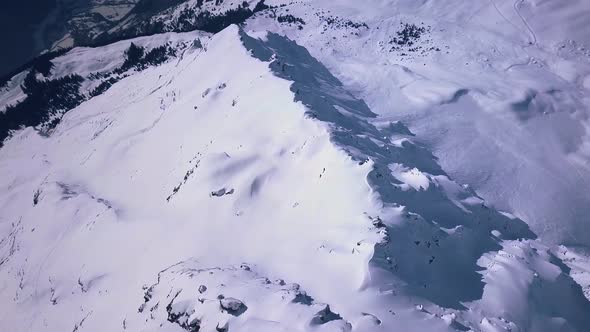 Aerial drone footage flying over the edge of a snowy mountain ridge above the ski resort town in Ver