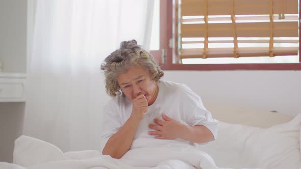 Asian Elderly woman with white hairs sneezing and coughing sit on bed alone at home