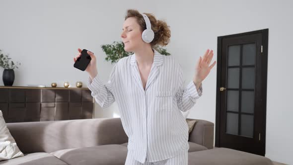 People And Technology Concept. Cheerful Girl Dancing In Living Room At Home Using Cell Phone.
