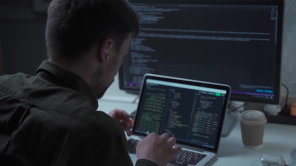 A Male Programmer Works at a Computer and Uses an Inear Headset to Talk with a Colleague or Customer