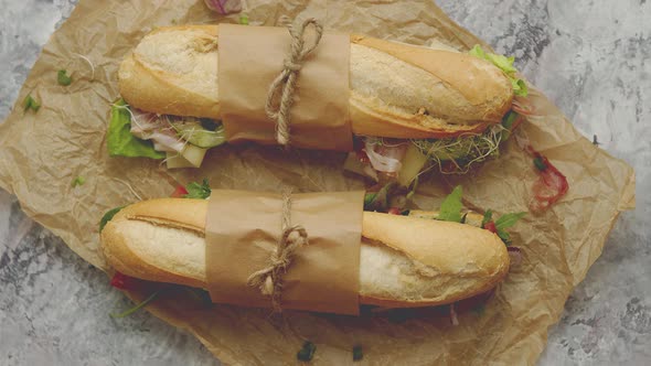 Sandwiches with Ham, Fresh Vegetables and Herbs Served on Brown Baking Paper Over Concrete Backdrop