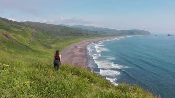 Young Woman Looking at the Ocean Standing on a High Cliff Above the Sandy Beach