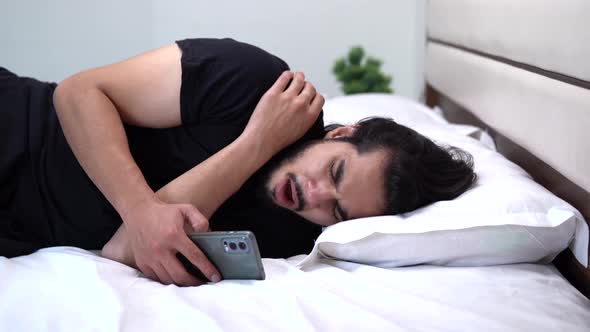 Tired Indian man using the phone on the bed