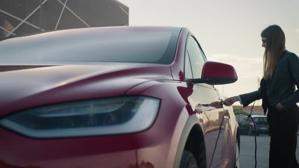 Young Beautiful Stylish Girl Approaches a Luxurious Modern Electric Car Which is