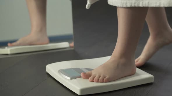 Extra weight, fat female in bathrobe stepping on scales to check diet results