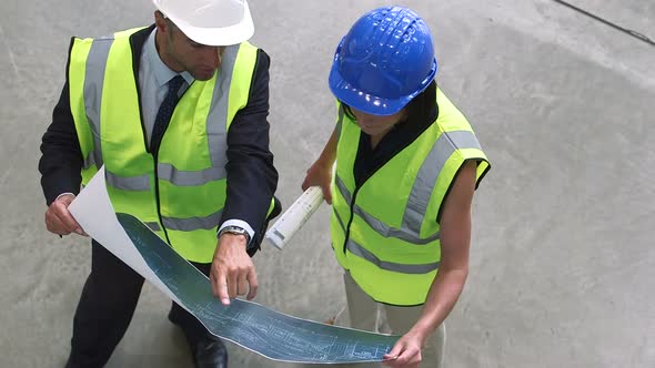 Man and woman discussing with blueprint at construction site