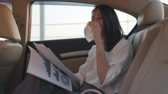 young Asia businesswoman working and drinking disposable paper cup of hot drink in back seat.