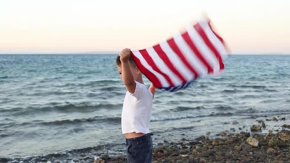 boy waving national USA flag at sea over the blue sky