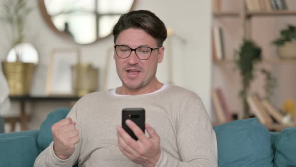 Middle Aged Man Celebrating on Smartphone at Home 