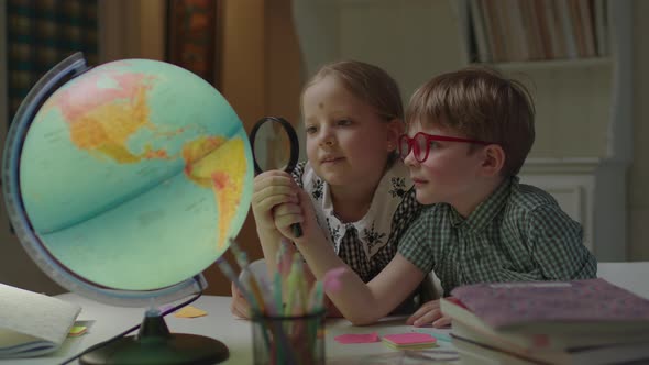 Two Kids Studying Earth Globe with Magnifying Glass