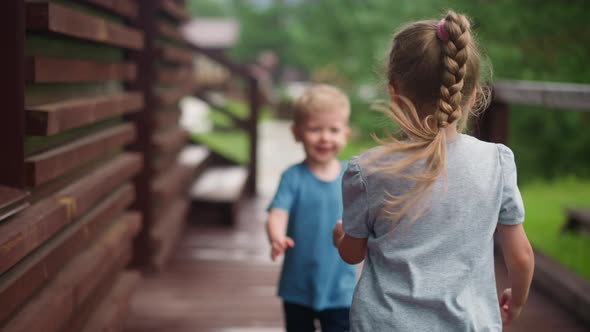 Little Girl Runs Playing with Funny Brother on Veranda Deck