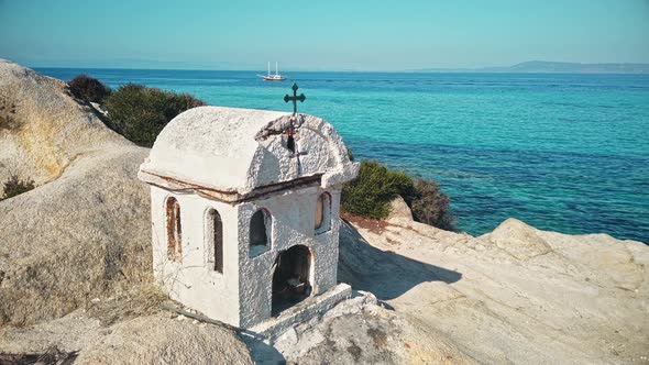 A small shrine located on rocks near the Aegean sea coast, water and moving yacht on the background,