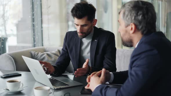 Senior Executives Talking in Cafe at Table with Laptop Discussing Contract