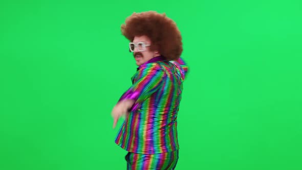 A Retro Dude in a Funny Wig and Multicolored Suit is Dancing a Funny Spinning Dance on a Green