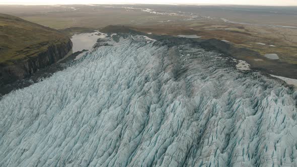 Large glacier in Iceland flowing down mountain to green plains. Aerial tilt up.