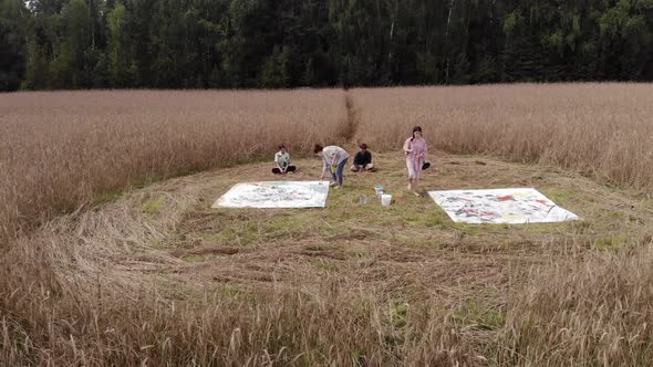 Drone Shooting of Young Girls Drawing Pictures on Canvases in a Circle on a Wheat Field