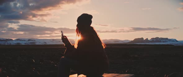 Person sits during sunset while on phone