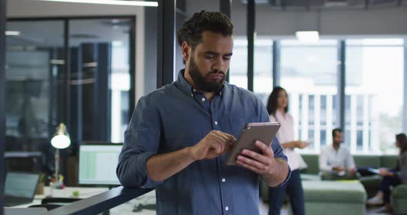 Smiling mixed race businessman standing in office using tablet and looking up to camera