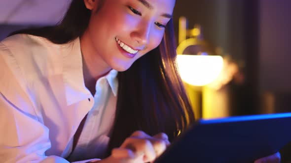 Young Asian beautiful woman enjoy using smartphone- tablet   in bedroom at night time.