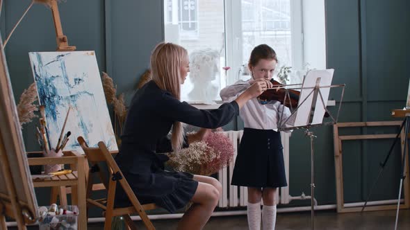 Young Blonde Woman Teacher Teaching a Little Girl How to Properly Hold a Bow While Playing Violin