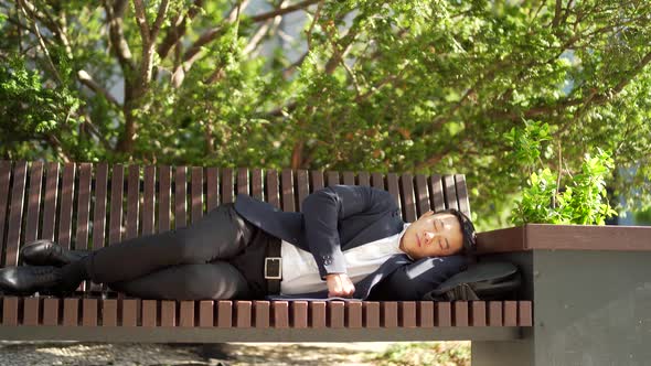 exhausted and overworked young asian businessman lying on a bench in the city central park outdoors.