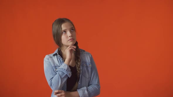 A Young Girl Looks Thoughtfully Up in an Orange Background