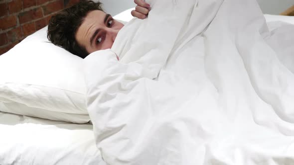 Young Man Peeking Out From Blanket in Bed