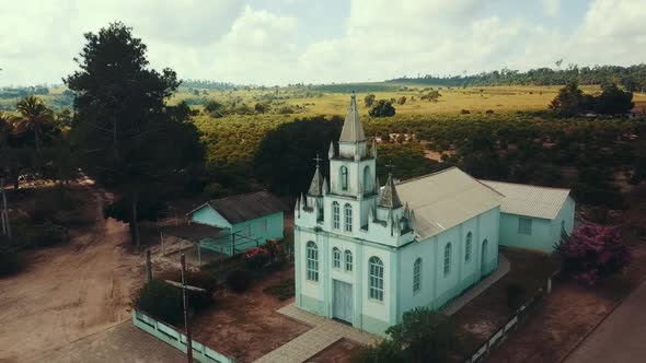 Aerial drone shot flies towards a small white church in a rural village in South America