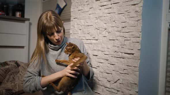 Young Woman Playing with Cute Abyssinian Cat or Kitten at Home Against White Wall