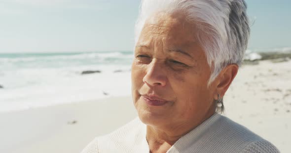 Portrait of thoughtful senior hispanic woman standing on beach and look into distance