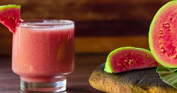 Glass of red guava juice and sliced guava slice on wooden background