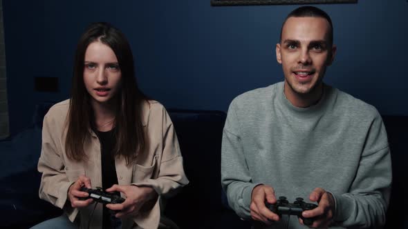 Excited Couple Playing Video Games While Sitting on Sofa in Front of Tv at Home. Young Man and Woman