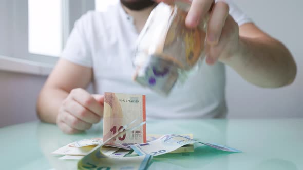 Close Up of a Hands of Man Taking Money Out of His Glass Bank