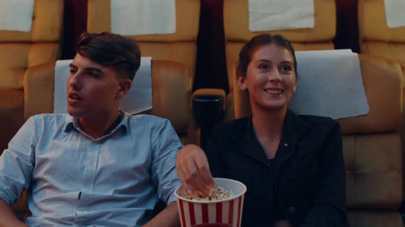 Attractive cheerful young caucasian couple laughing while watching film in movie theater.