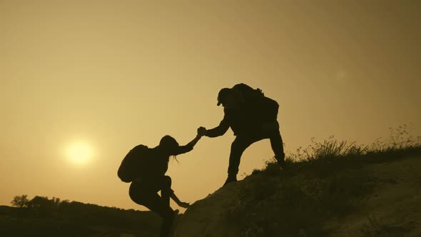 Silhouette of Helping Hand Between Two Climber. Two Hikers on Top of the Mountain, a Man Helps a