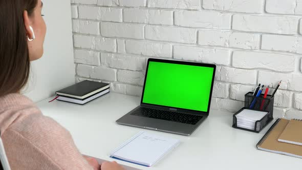 Woman student at home nods head listens teacher tutor with green screen laptop