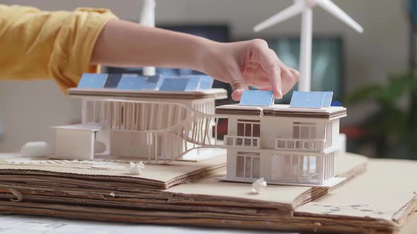 Close Up Of Woman'S Hand Putting The Solar Panel On The Roof Of A Small Model House