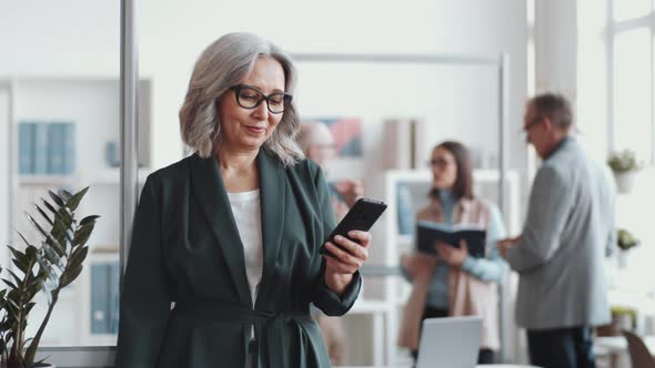 Attractive Senior Businesswoman Using Smartphone and Posing for Camera