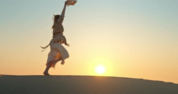 Happy Excited Woman Running By Sand Dune with Golden Sunset on Background