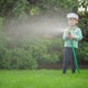 A Small Child is Watering the Plants Near the House with a Hose - VideoHive Item for Sale