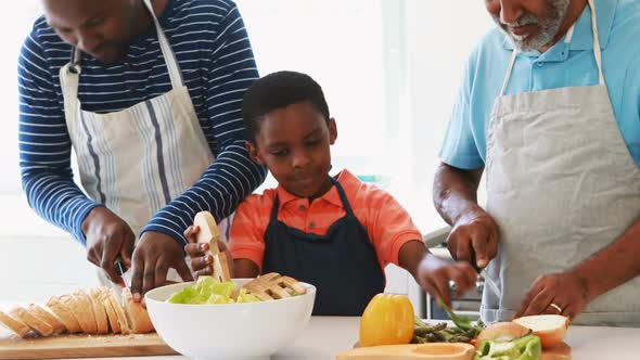 Boy preparing salad with his father and grandfather