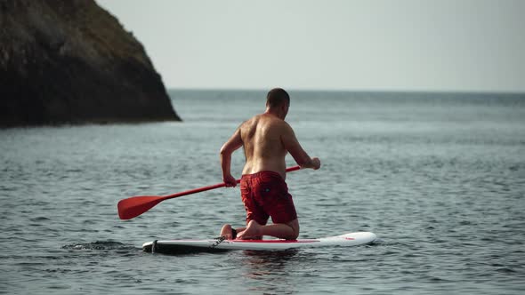 Middle Aged Man Riding SUP Surf Longboard at Seaside Resort Active Fun on Water