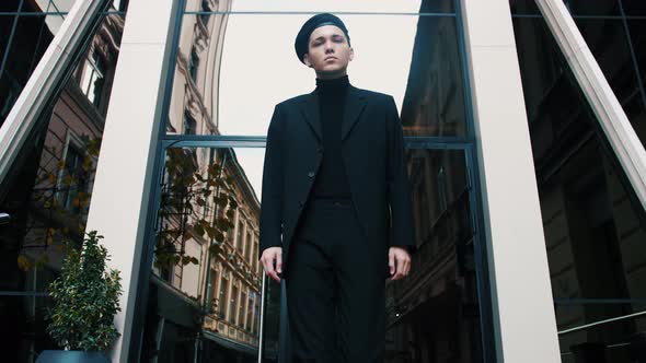 Confident and Handsome Young Businessman with Beret Walking Down Modern City Street and Looking Away