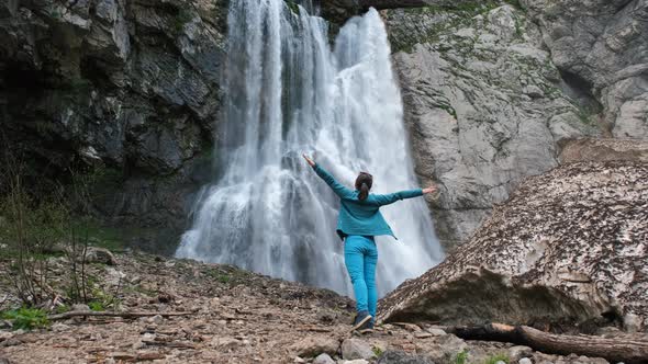 Woman Standing Near Waterfall with Hands Raised