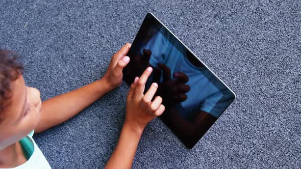 Schoolboy lying on floor and using digital tablet in library at school