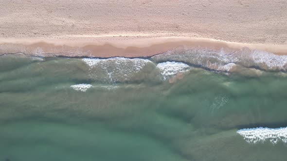 Static top down view of tropical beach, foamy ocean waves washing sand.