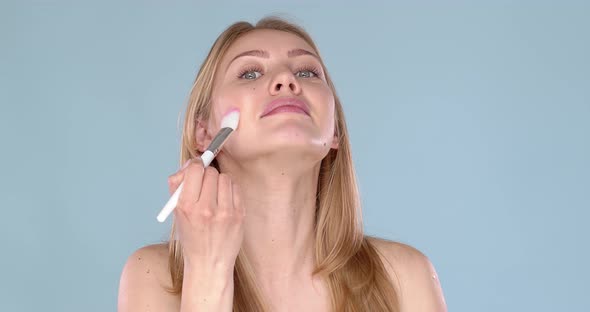 Beautiful Blond Woman Applying Makeup Powder on Her Face Using Brush