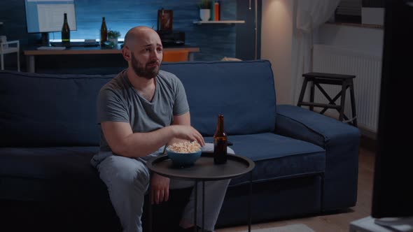 Focused Man Looking at Drama Movie Crying Sitting on Sofa Eating Popcorn