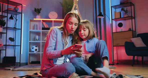 two diverse sisters sitting on the coverlet at home in the evening and use phone