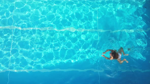 Young Woman Enjoys Swimming in the Cool Water of a Pool in Summertime